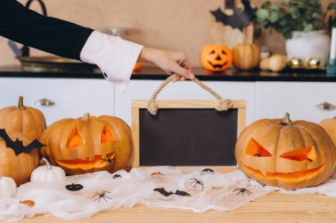 Halloween composition with pumpkins, spiderwebs, spiders and bats with a woman holding an empty blackboard with copy space