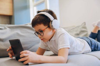 Child enjoying digital entertainment on a tablet, wearing headphones and eyeglasses, promoting concepts of childhood, technology, and leisure
