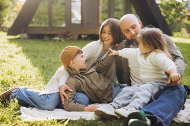 Happy family relaxing and having fun sitting on a blanket in their garden, enjoying quality time together