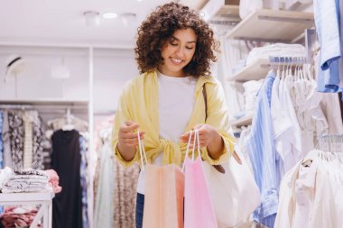Smiling customer admiring colorful shopping bags while enjoying a day of retail therapy in a trendy fashion store
