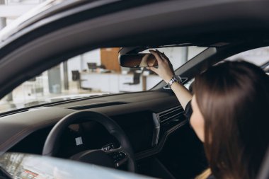 Woman adjusting rearview mirror while sitting in new car at dealership showroom