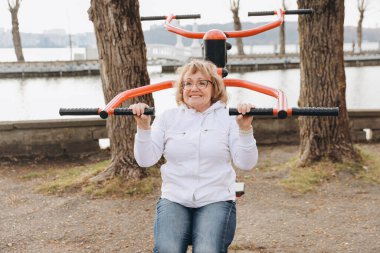 Happy senior woman exercising on outdoor gym equipment, enjoying active lifestyle and staying fit