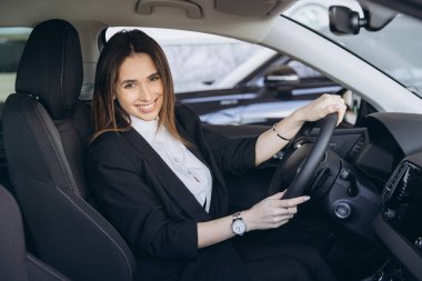 Smiling businesswoman sitting at steering wheel of car, testing vehicle before purchase in car dealership