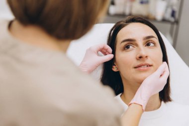 Cosmetologist wearing pink gloves examining woman's face and making markings before botulinum toxin injections in beauty clinic