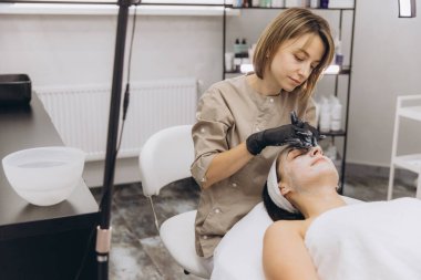 Beautician wearing black gloves applying a facial mask to a client lying on a massage table in a professional beauty salon