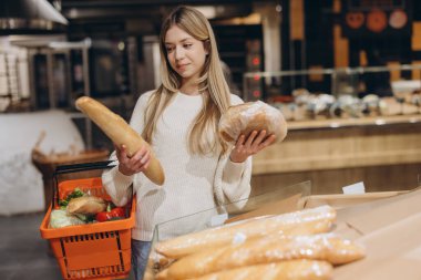 Müşteri, markette alışveriş yaparken çeşitli taze ekmek türlerini karşılaştırarak sağlıklı bir yemek seçeneklerini değerlendiriyor.