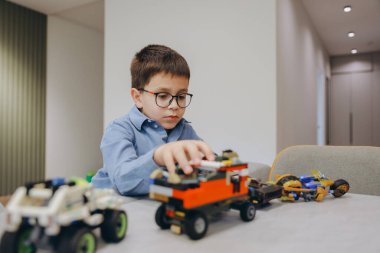 Young boy concentrating on building a toy car with colorful plastic bricks, developing his creativity and problem solving skills in a comfortable home environment