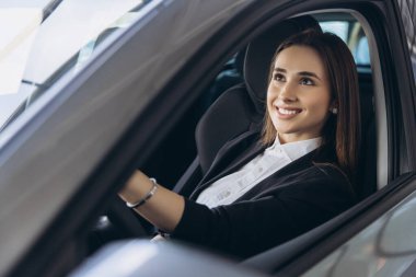 Saleswoman smiling while seated in a new car, relishing the experience at the car dealership, embracing the excitement of ownership