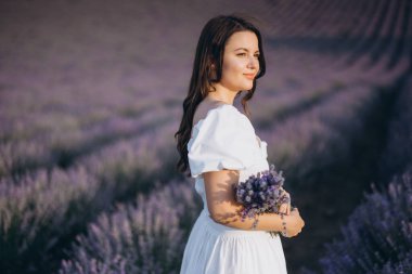 Young woman wearing a white dress holding a bouquet of lavender in a lavender field during a sunny day