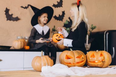 Mother and daughter carving pumpkins together, getting ready for a Halloween party, wearing costumes
