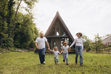Happy family running on grass in front of their a frame house, enjoying their vacation in nature