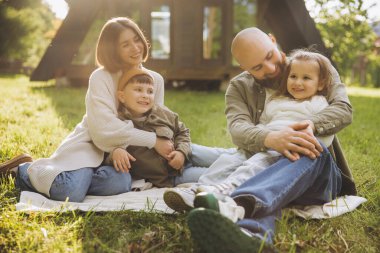 Smiling family sitting together on a cozy blanket in the backyard, enjoying quality time and embracing the warmth of each others company