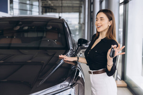 Saleswoman showing car keys while gently touching a new car in a dealership