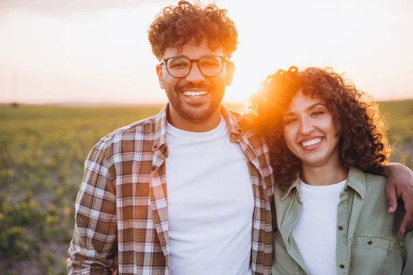 Two agronomists hugging and smiling in a soybean field at sunset, enjoying the fruits of their labor