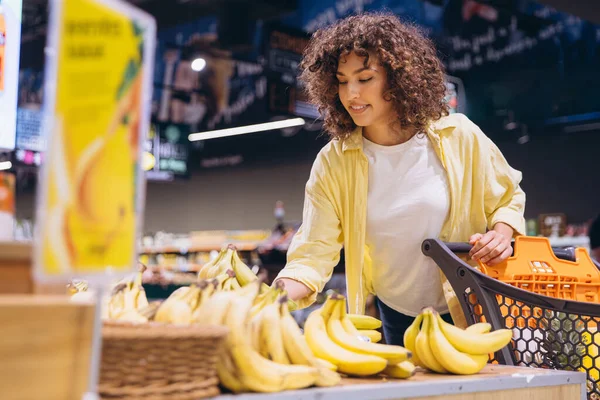 Customer buying groceries selecting fresh produce reaching for bananas in supermarket aisle, healthy eating and consumerism concept