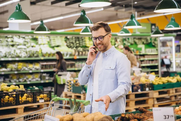 Customer choosing potatoes while using mobile phone in grocery store