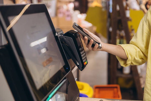 Shopper using smartphone to make a contactless payment at a supermarket checkout, utilizing NFC technology for a quick and convenient transaction