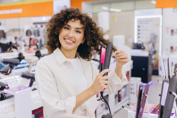 Smiling woman testing new hair straightener in electronics store, choosing best hair care product