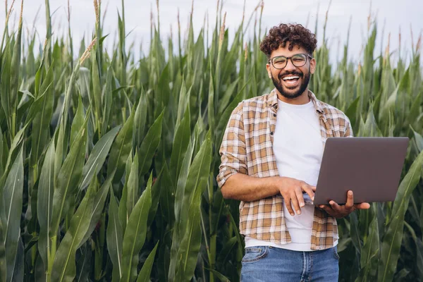 Arab agronomist smiling and working with laptop in a corn field, agriculture and technology concept