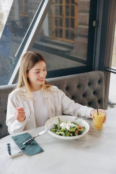 Young businesswoman enjoying a healthy lunch break with a fresh salad and orange juice, promoting a balanced lifestyle in a modern restaurant setting