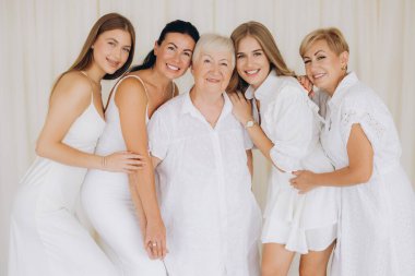 Five women of different ages, wearing elegant white dresses, are posing together, creating a beautiful family portrait