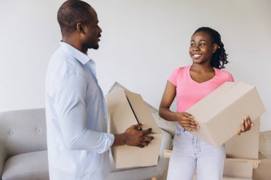 Smiling couple carrying cardboard boxes, joyfully moving into their new home, embracing the excitement of fresh beginnings together