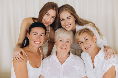 Five women of different ages, from young girls to elderly grandmother, posing together with a cheerful smile, showing family unity and love