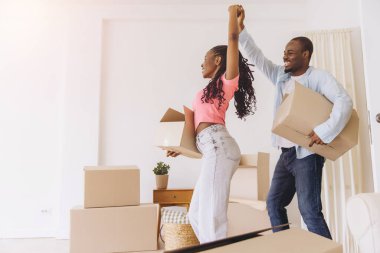 Young black husband and wife are having fun while carrying cardboard boxes in their new apartment