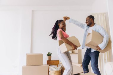 Young black couple is moving in a new house, dancing and having fun together while carrying cardboard boxes