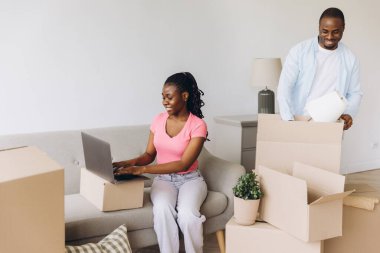 Happy African American couple moving into a new home, joyfully unpacking boxes and organizing their belongings in a bright, spacious apartment