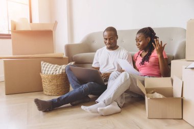 Happy african american couple sitting on the floor and organizing their move with a laptop and documents