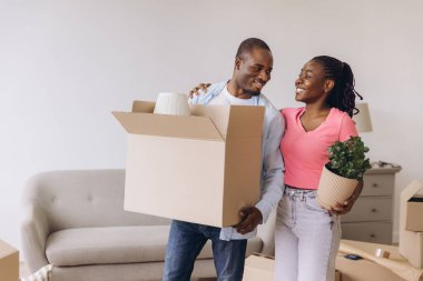 Smiling african american couple carrying belongings in cardboard boxes moving into new apartment