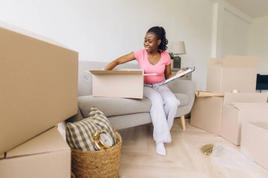 Happy african american homeowner unpacking boxes in a bright living room, enjoying the excitement of settling into a new house and making it a home