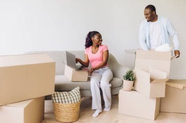 Young African American couple unpacking boxes and using laptop in new apartment, starting new life together