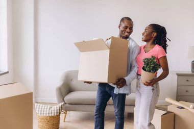 Smiling african american couple carrying belongings into new home, starting a new chapter together