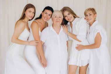Four generations of women in white dresses posing together in a bright interior, radiating love, connection, and family unity