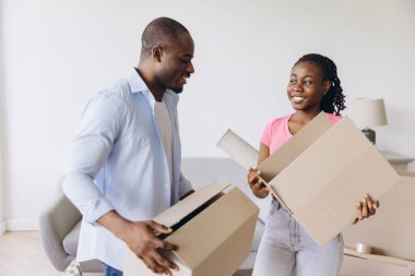 Smiling couple moving into a new house, carrying cardboard boxes and unpacking their belongings