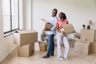 Smiling couple carrying cardboard boxes, joyfully moving into their new home, embracing the excitement of fresh beginnings together
