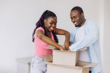 Young smiling african american couple unpacking belongings from cardboard boxes in new apartment