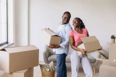 Smiling couple carrying cardboard boxes, joyfully moving into their new apartment and embracing the excitement of fresh beginnings together