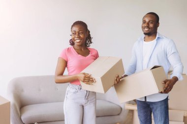 Smiling African American couple carrying cardboard boxes while moving into their new home, embracing a fresh start filled with excitement