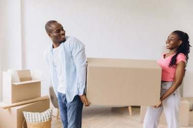 Smiling African American couple carrying a large cardboard box while moving into their new home, embracing the excitement of fresh beginnings