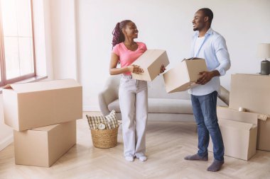 Smiling African American couple carrying cardboard boxes while moving into their new home, excitedly beginning their journey together