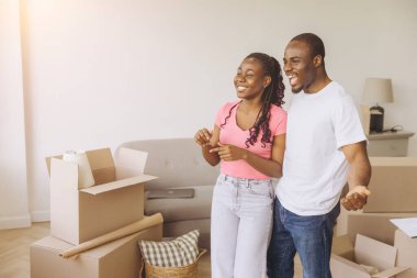 Excited african american couple visualizing furniture placement in new apartment, surrounded by cardboard boxes