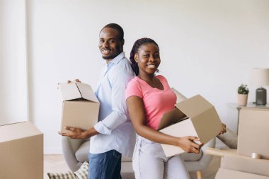 Smiling couple carrying cardboard boxes while moving into their new apartment, excitedly starting fresh and embracing new beginnings together