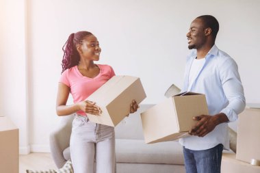 Smiling African American couple carrying cardboard boxes while moving into their new home, embracing a joyful beginning in their lives together