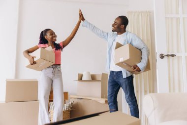 Smiling african american couple is giving high five while carrying cardboard boxes and moving into new apartment