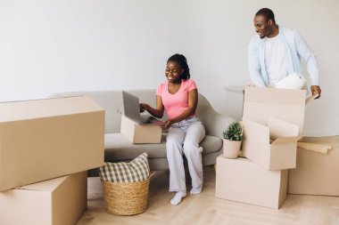 Happy African American couple unpacking boxes and using laptop in their new apartment, excited about starting a new chapter in their lives together