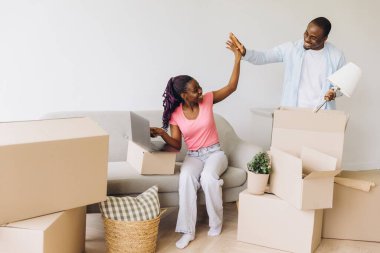 Young black couple moving into a new apartment, unpacking boxes, sharing high fives, and celebrating their fresh start together