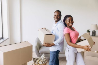 Young African American couple joyfully carrying cardboard boxes while moving into their new apartment, embracing a fresh start together